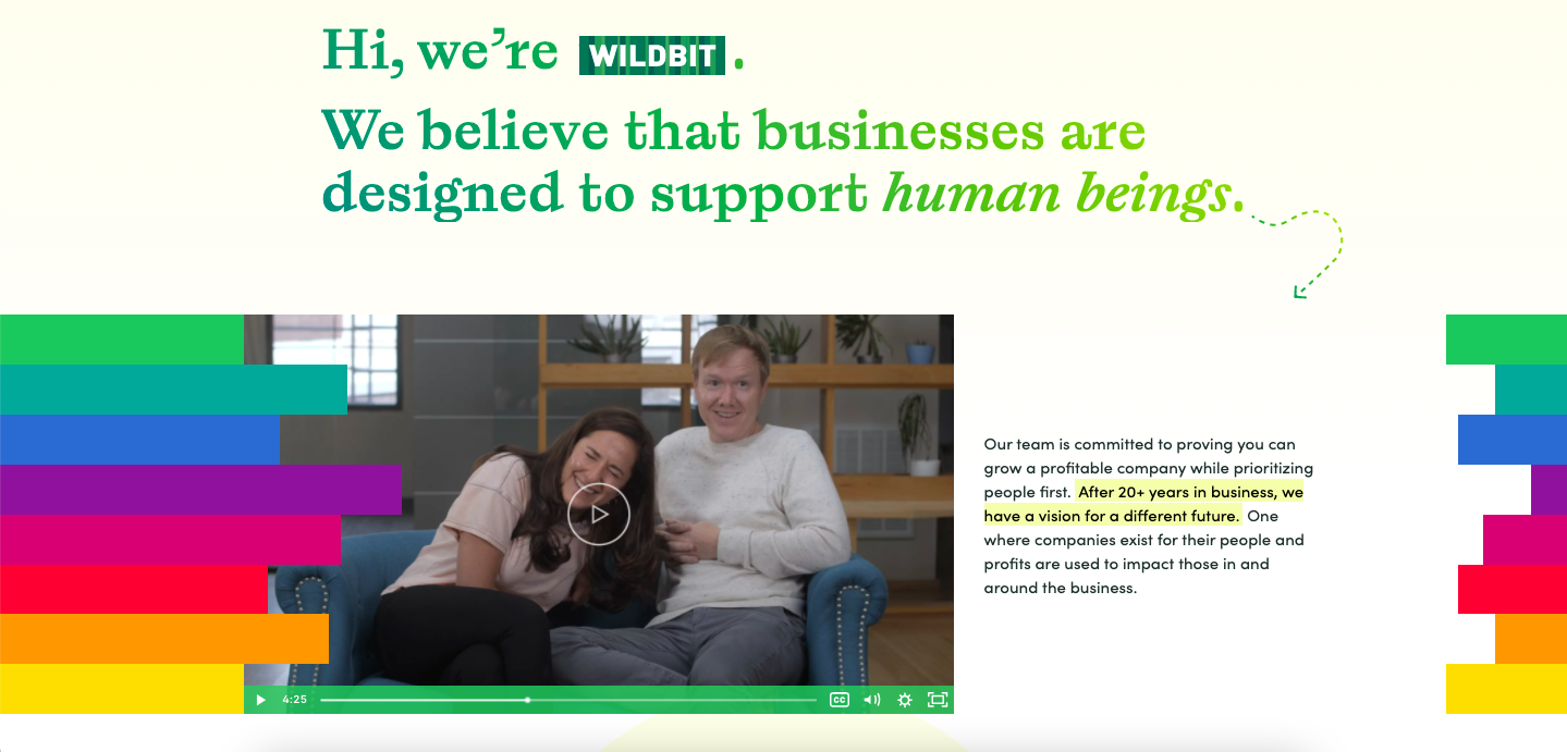 A video embedded on the Wildbit landing page of two people sitting in a chair laughing, with text to the right of the video, and rainbow stripes on the right and left borders. 