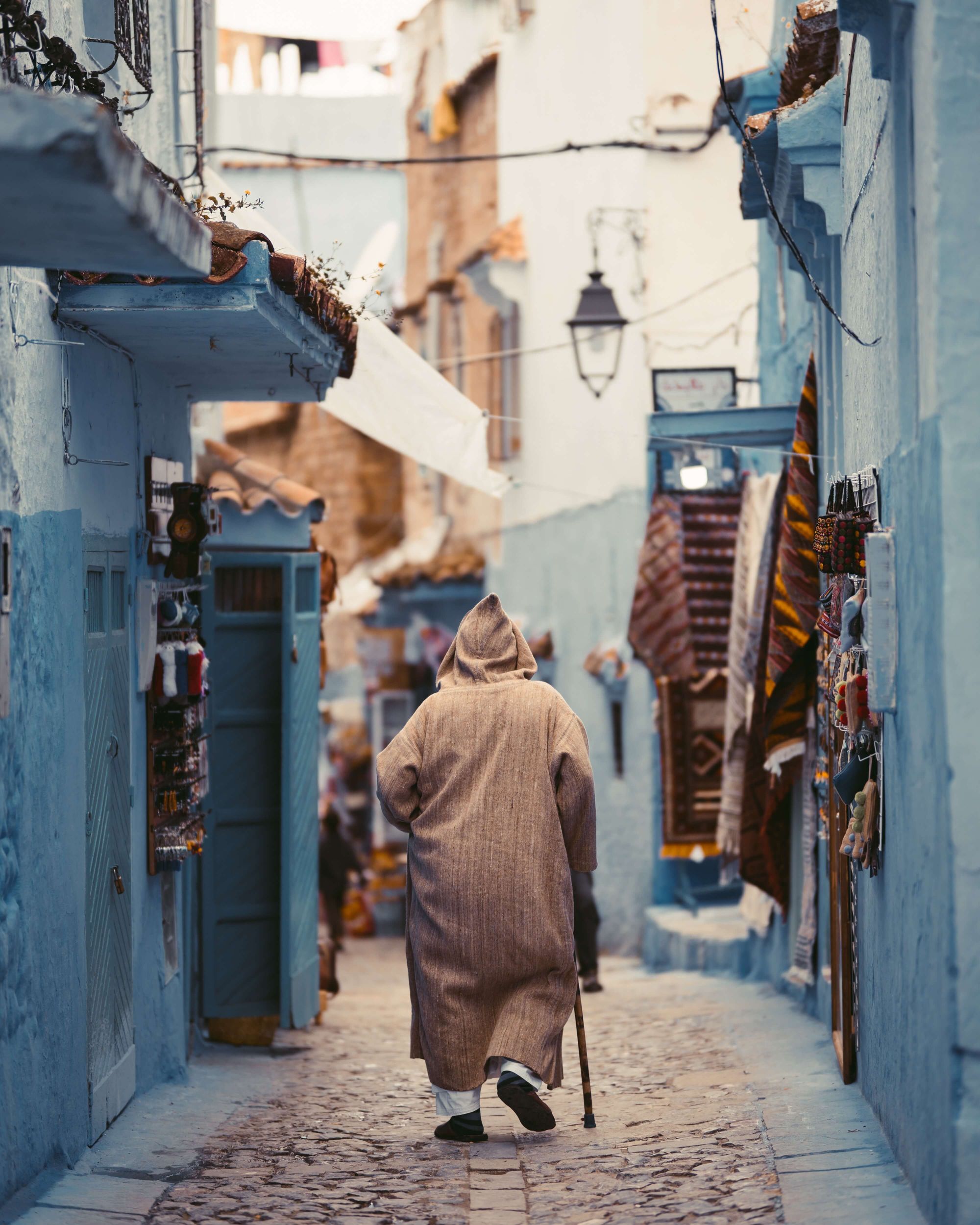 A man walking with a cane wearing a Moroccan Djellbass