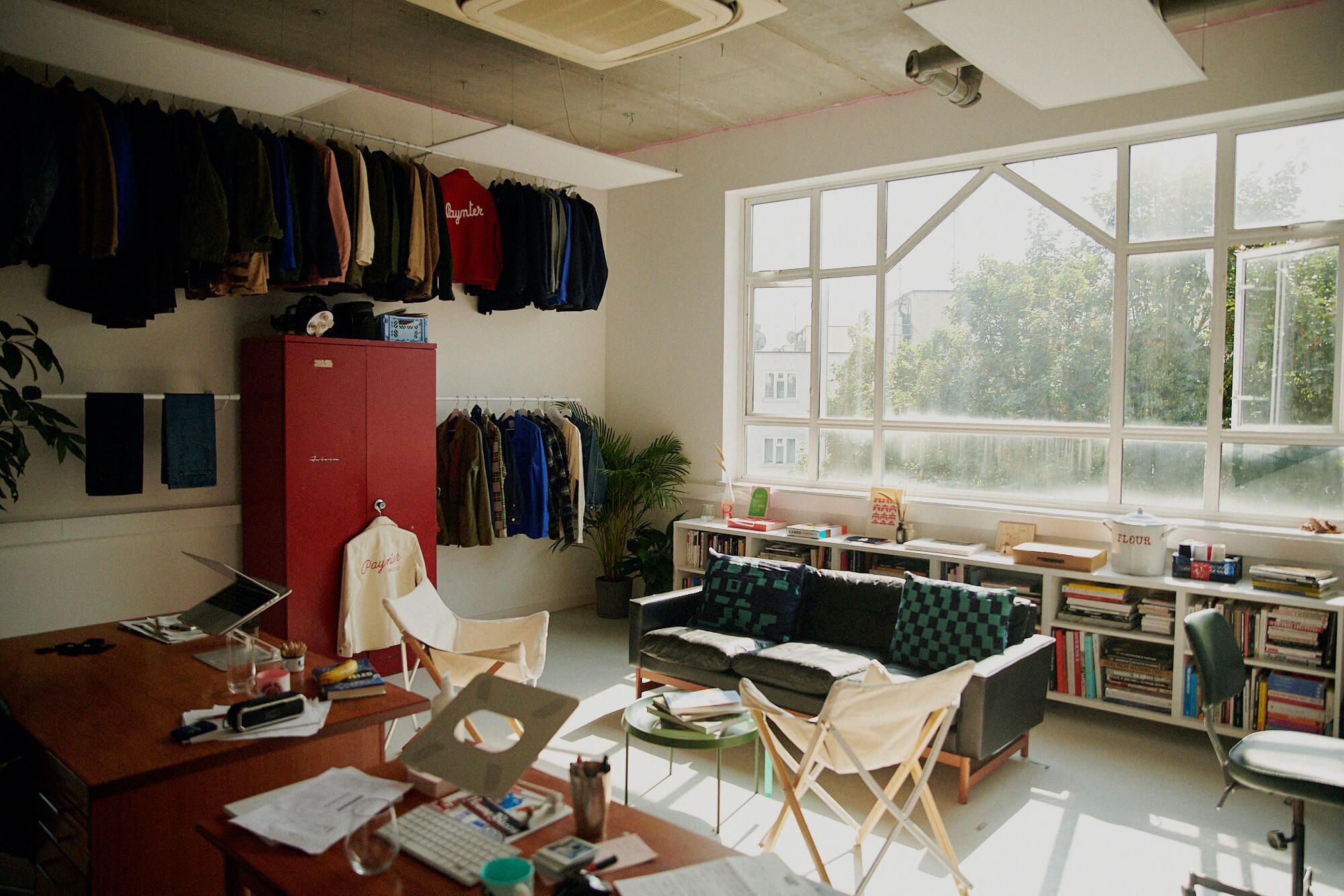 A clothing studio with a desk, sofa, and jackets hanging on the side.