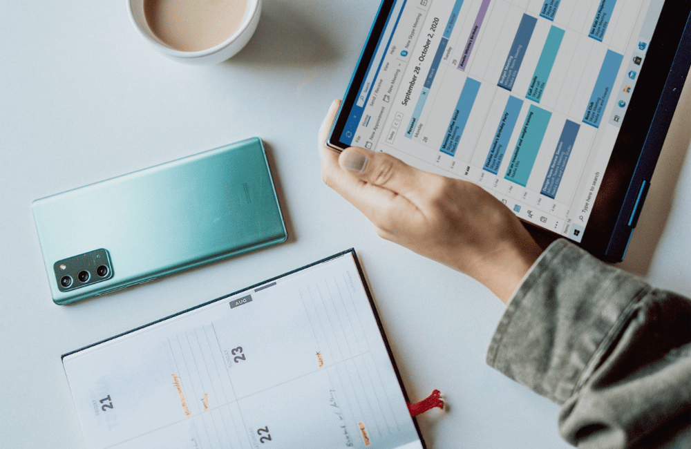 Person planning their social media calendar for 2024 holding tablet while referencing a diary.