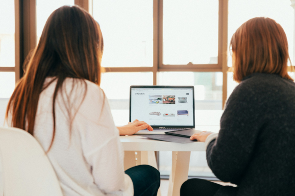 Two women examining a laptop to indicate deciding between social media management tools and sprout social alternatives.