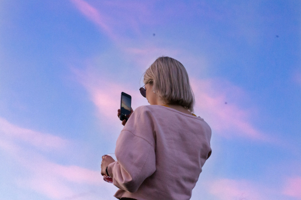 A woman filming a video of the sunset where the clouds are turning pink, to illustrate someone creating on TikTok Studio