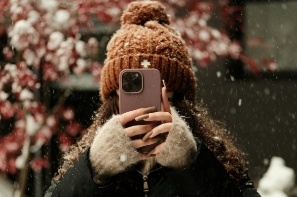 woman in beanie hat taking a photo with her phone in the show, to indicate reposting on Instagram