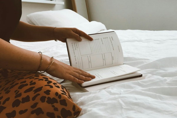 Woman sitting on bed turning pages in her diary to indicate a business owner creating thought leadership content