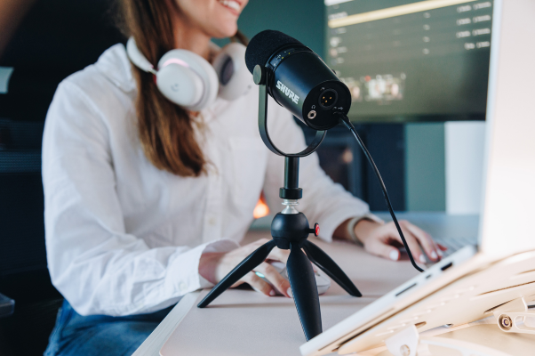 Woman sits at a desk in a home office with a microphone in the foregroudn editing a video on her computer for TikTok