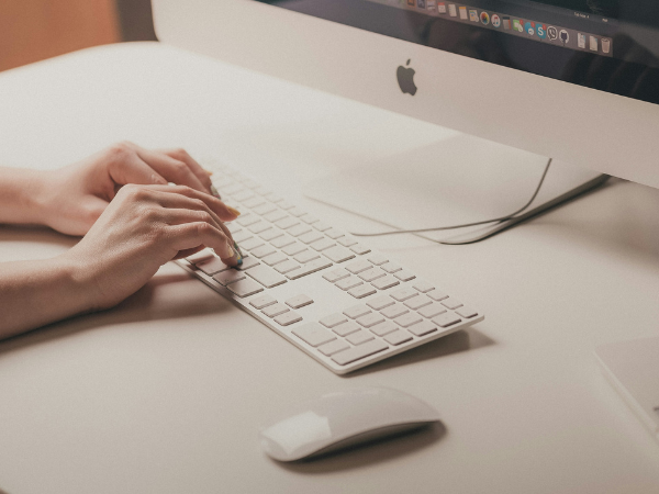 Hands type on a white keyboard atop a white desk, with a mouse nearby to illustrate searching for the best URL shortener