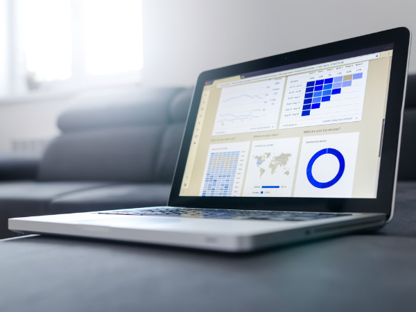 A laptop sits open on a grey table with graphs visible on the screen to indicate social media analytics tools