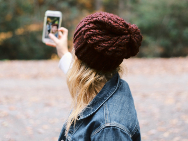 A woman in a beanie hat takes a selfie with her phone, to illustrate using Instagram stories