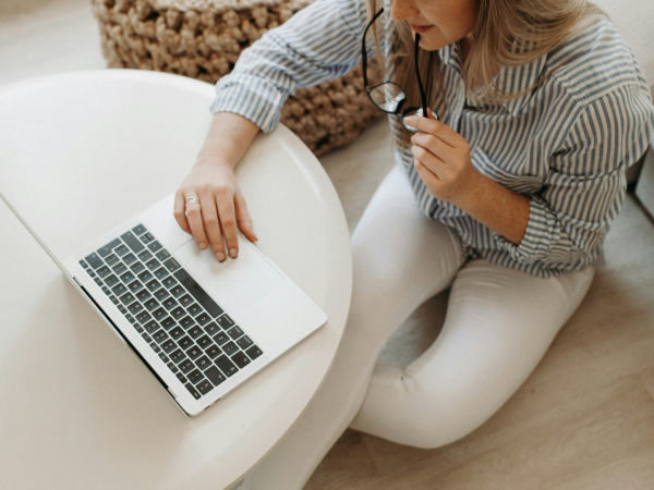 A woman sits on the floor working on her macbook open on a coffee table