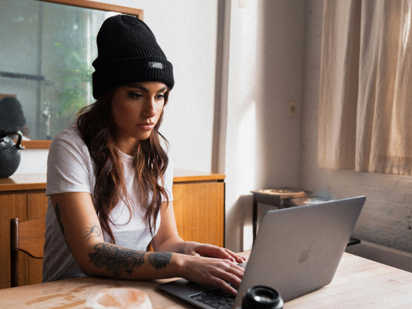 A woman in a black beanie sits at a desk working on a macbook to illustrate social media content creation