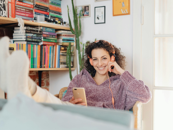 A woman sits in her office with her feet up on her desk listening to music on her phone with headphones to illustrate rending Instagram Audio