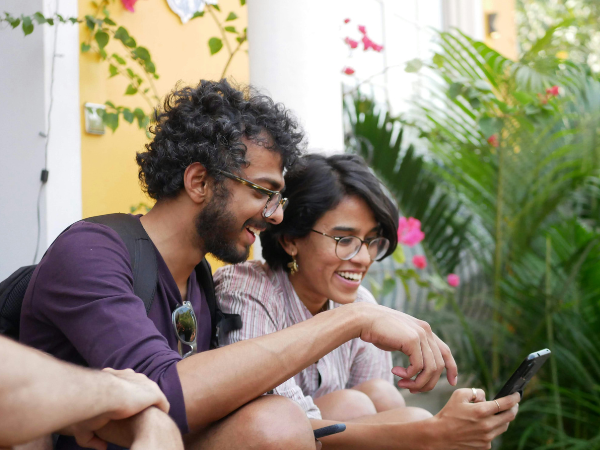 Two friends sitting outdoors, smiling and looking at a phone together, surrounded by greenery and flowers to illustrate Instagram Friends M
