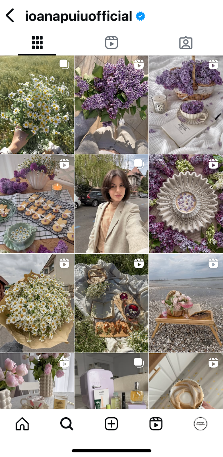 Instagram profile grid showing a soft, floral aesthetic with daisies, lilacs, styled picnics, baked goods, and cozy home scenes in pastel tones. Posts alternate between photos and Reels.